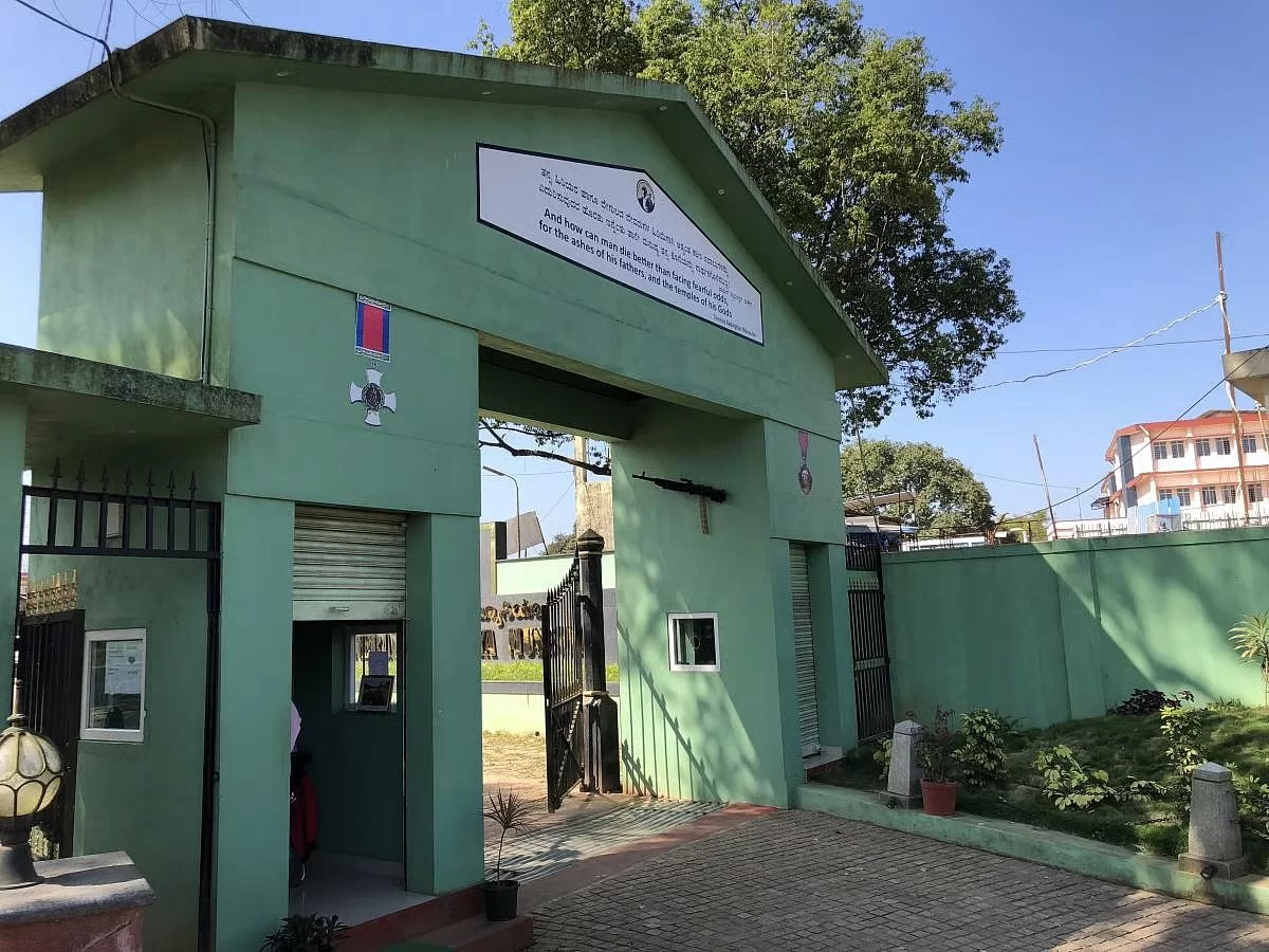 General Thimayya Memorial Museum gate at Madikeri Coorg during sunny day, featuring green arch, medals, portrait, trees, perfect cultural experience Karnataka tour packages.