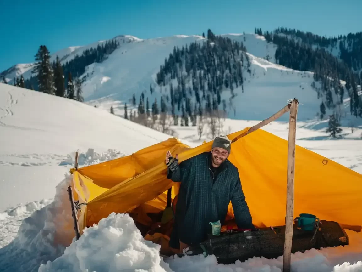 Gulmarg Kashmir orange tent snow slope man smiling cap jacket mug snowy mountains pine trees blue skies, perfect winter camping adventure ski tour package.