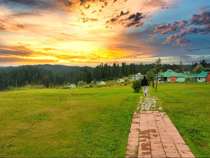 Gulmarg Kashmir sunset orange purple sky green meadows stone path walking man green red huts pine forests mountains, perfect golden hour highland serenity tour package.