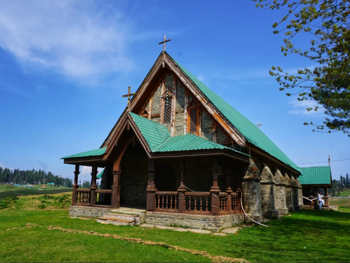 Gulmarg Kashmir green roof wooden church cross stone walls balcony pine trees green grass blue skies mountains, perfect Christian heritage alpine spiritual tour package.