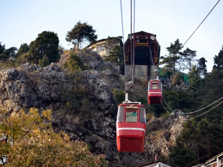 Gun Hill in Mussoorie, Uttarakhand with red cable car rides ascending the rocky hillside, a popular viewpoint included in Uttarakhand tour packages