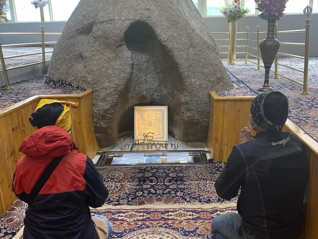 Sacred Pathar Sahib boulder shrine at Gurdwara Pathar Sahib Leh Ladakh featuring miracle rock with embedded Guru Granth Sahib replica devotees in prayer floral decorations brass railings and ornate carpet, revered Sikh spiritual Ladakh tour package must-v