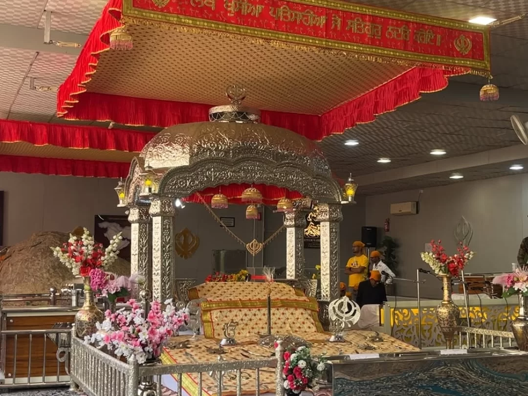 Guru Granth Sahib palanquin shrine at Gurdwara Shri Pathar Sahib Leh Ladakh with red golden canopy Punjabi banner Khanda symbols floral decorations brass stands wooden walls swords photos, devotional Sikh holy book palanquin Ladakh tour package focal poin