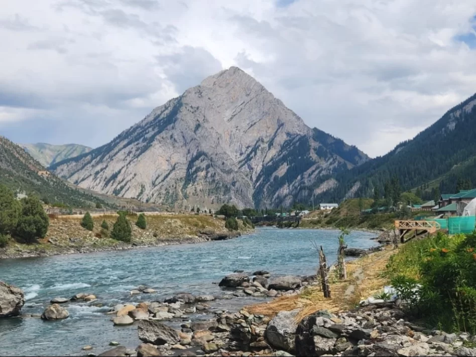 Majestic Habba Khatoon Peak at Gurez Valley during cloudy weather, featuring turquoise river and villages, perfect adventure Srinagar tour package. 