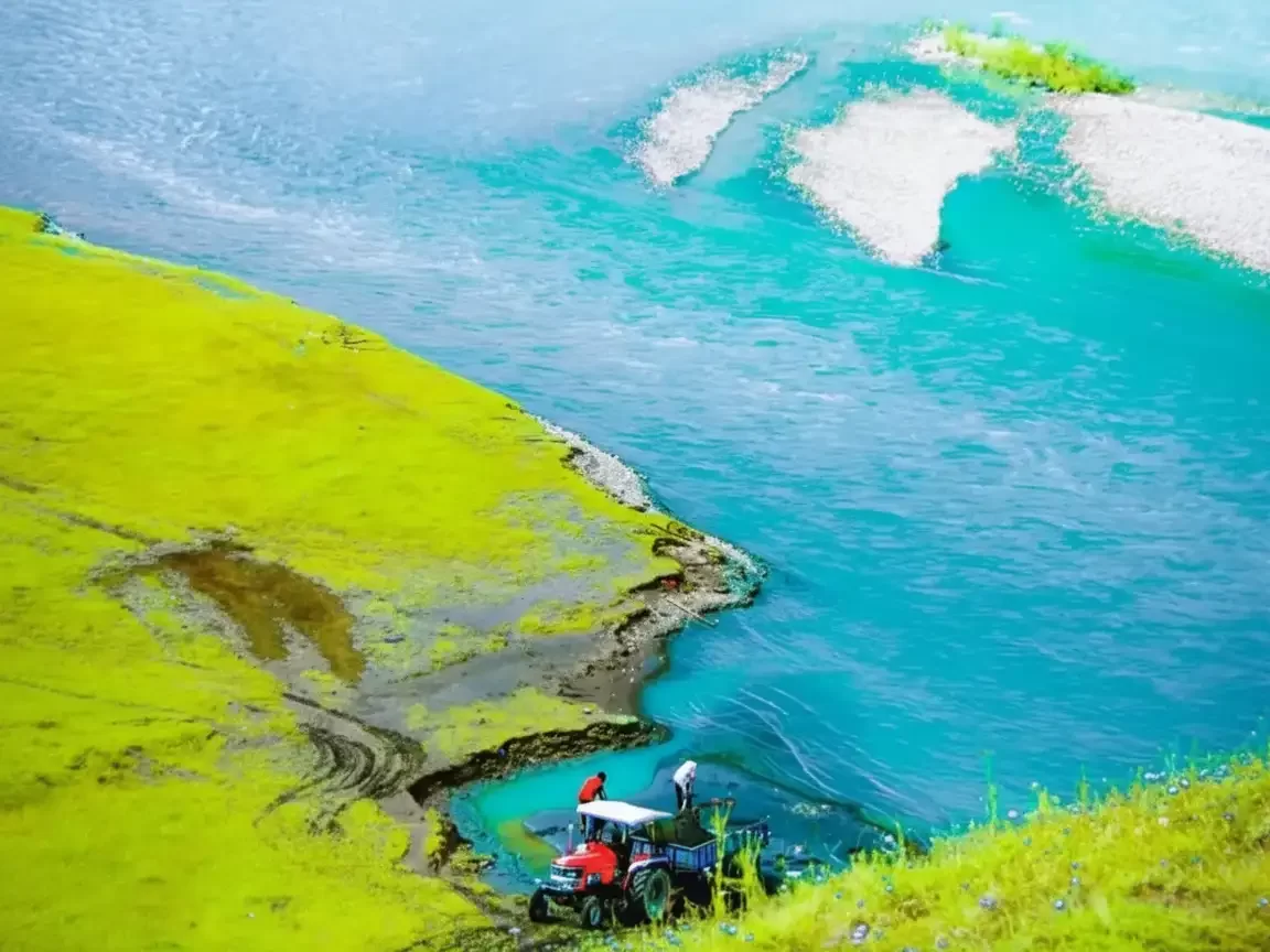 Tractor ride at Gurez Valley during clear skies, featuring turquoise river and lush green meadows, perfect adventure experience Srinagar tour package. 
