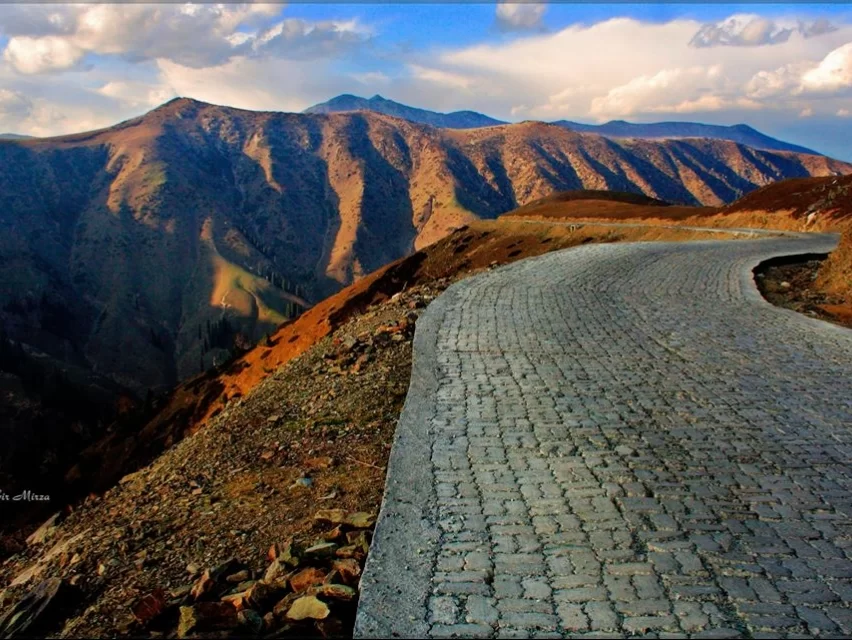 Winding road at Gurez Valley during golden hour sunset, featuring rugged brown mountains and rocky terrain, perfect adventure experience Gurez tour package. 