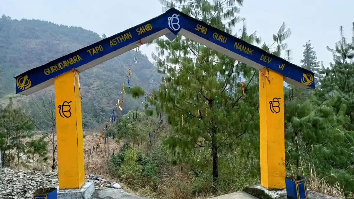 Gurudwara Tapo Asthan Sahib in Menchuka featuring blue-yellow entry arch, pine trees, and serene valley, perfect Arunachal Pradesh tour package experience.