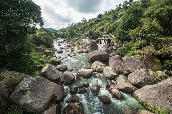 Jakrem Hot Springs near Shillong featuring a rocky riverbed, flowing natural stream, and lush green hillsides, perfect wellness experience with Meghalaya tour package.