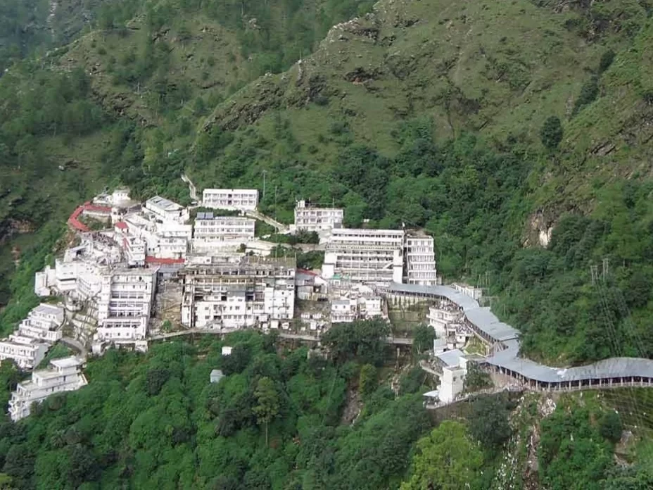 Vaishno Devi Bhawan aerial view Katra misty day, featuring white buildings red roofs forested Trikuta slopes walkways, perfect pilgrimage experience Jammu Kashmir tour packages.