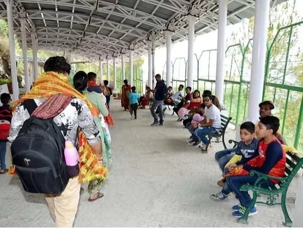 Pilgrims families waiting Katra railway station Jammu Kashmir daytime, featuring saffron dupattas backpacks benches green railing hills backdrop Vaishno Devi yatra, perfect pilgrimage experience Jammu Kashmir tour packages.