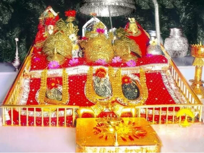 Ornate idols Mata Vaishno Devi shrine Katra Jammu Kashmir closeup, featuring three gold adorned deities red platform flowers lamps offerings, perfect pilgrimage experience Jammu Kashmir tour packages.