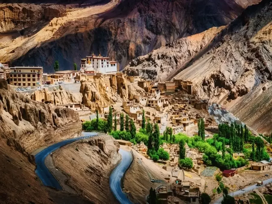 Lamayuru Monastery village Ladakh on moonscape cliffs at golden hour, featuring terraced buildings green trees and winding road, perfect spiritual Ladakh tour package.
