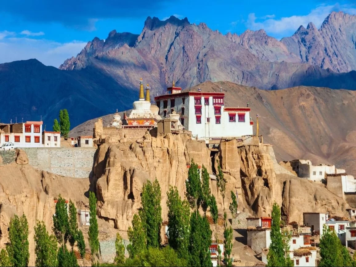 Lamayuru Monastery Ladakh atop rugged cliffs during partly cloudy skies, featuring white stupas cypress trees and jagged peaks, perfect spiritual Ladakh tour package.