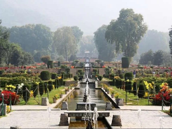 Vibrant flower beds and fountains at Nishat Garden Srinagar during misty morning, featuring chinar trees, hedges and central channel, perfect romantic experience in Srinagar tour package.