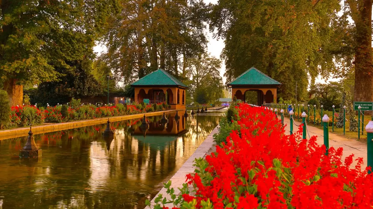 Green pavilions at Nishat Garden Srinagar during golden hour, featuring red flowers, canal reflections and chinar trees, perfect romantic experience in Srinagar tour package.
