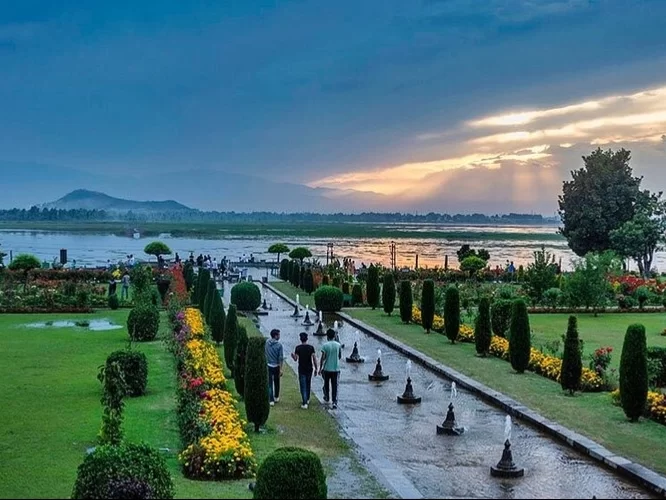 Visitors walking pathways at Nishat Garden Srinagar during sunset, featuring colorful flowers, Dal Lake, fountains and hills, perfect romantic experience in Srinagar tour package.