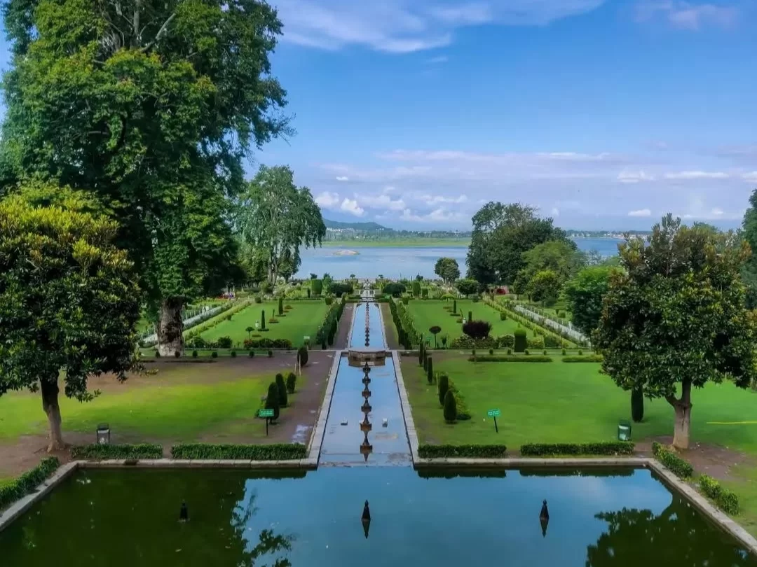 Terraced lawns and fountains at Nishat Garden Srinagar during sunny day, featuring Dal Lake, chinar trees and pool reflections, perfect romantic experience in Srinagar tour package.