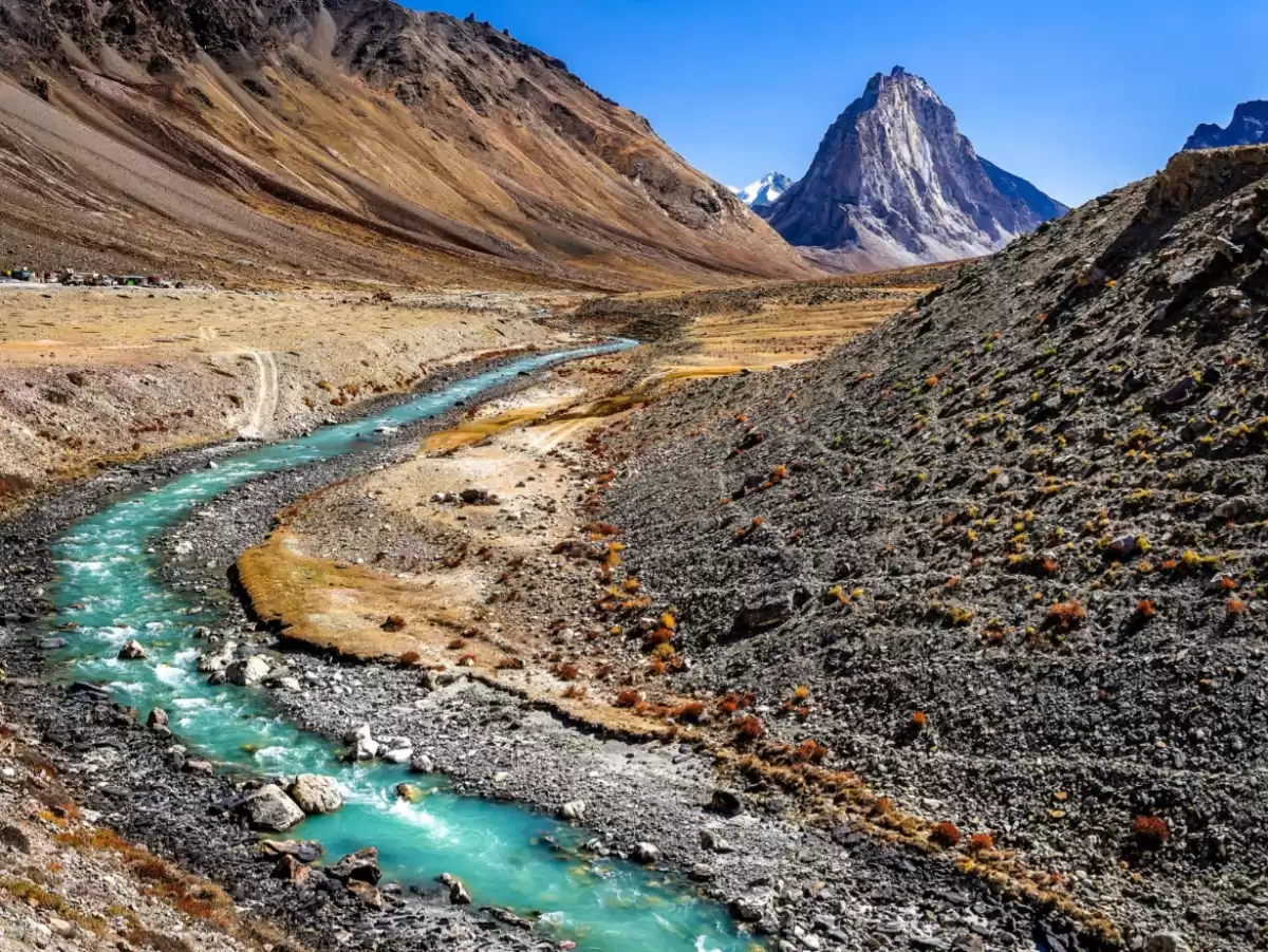 Scenic turquoise river valley near Padum village Zanskar Valley Ladakh during clear blue sky, featuring jagged snow peaks, barren mountains, perfect adventure Zanskar tour package. 