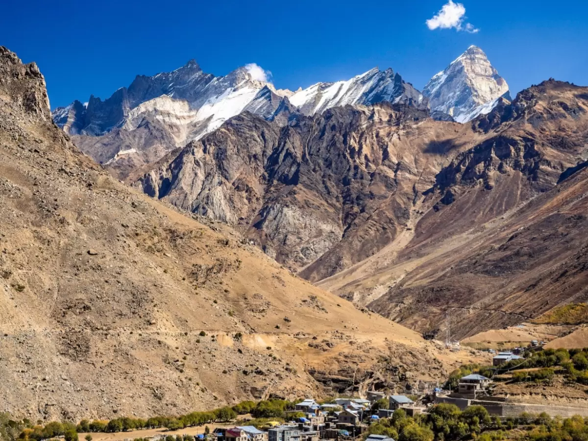 Padum Village Zanskar Ladakh aerial panoramic view colorful tin roof houses scattered valley snowcapped Nanga Parbat peak dramatic brown rugged mountains blue sky, high altitude remote village tour package.