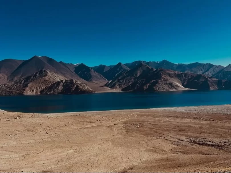 Ladakh Pangong Tso Lake turquoise blue brackish water terracotta brown rugged layered Himalayan mountains sandy beige shoreline clear blue sky high altitude panoramic scenic adventure trekking tour package Ladakh Himalayas