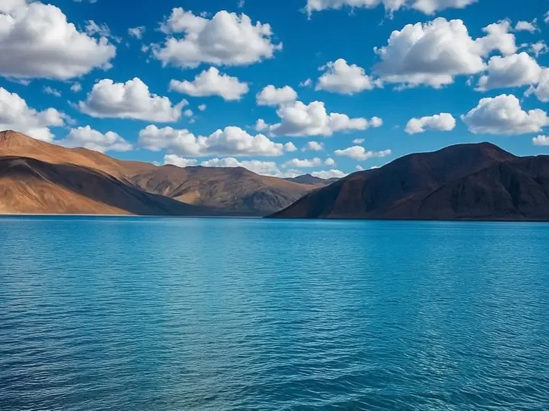 Ladakh Pangong Tso Lake turquoise blue brackish water terracotta brown rugged Himalayan mountains scattered white clouds clear blue sky panoramic high altitude landscape adventure tour package Ladakh Himalayas.