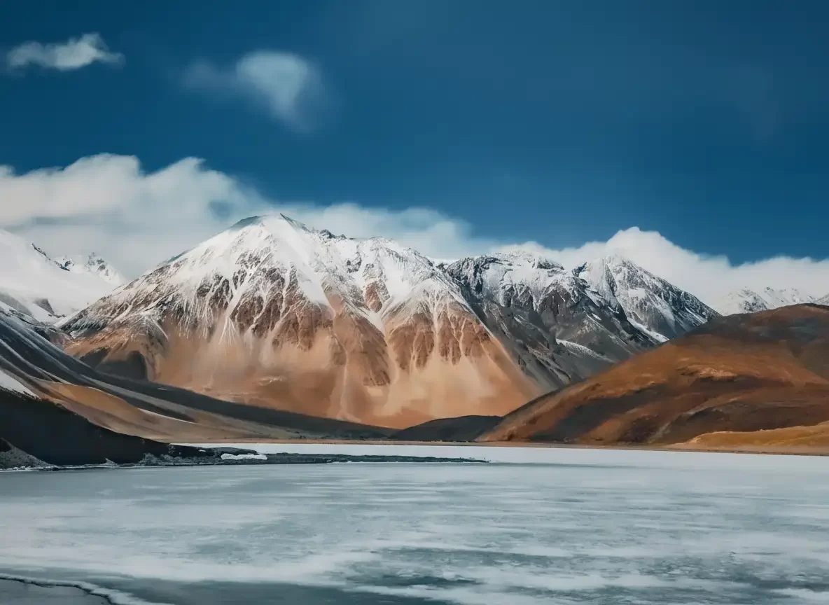 Majestic Pangong Lake at Pangong Tso Ladakh during winter sunny day, featuring towering snow mountains and frozen turquoise waters, perfect adventure Ladakh tour package.