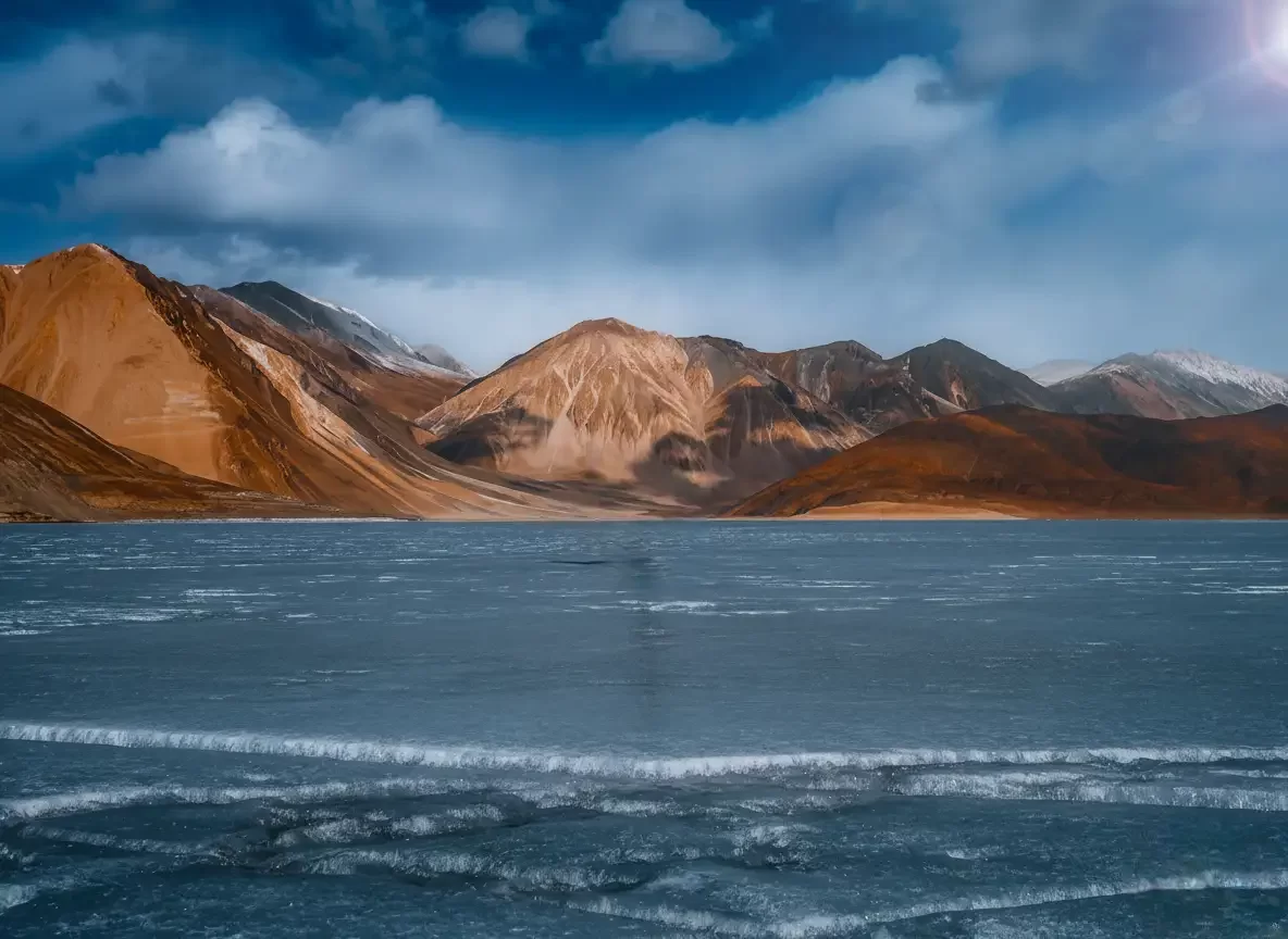 Pangong Lake at Pangong Tso Ladakh during winter golden hour, featuring terraced mountains and icy blue waters, perfect adventure Ladakh tour package. 