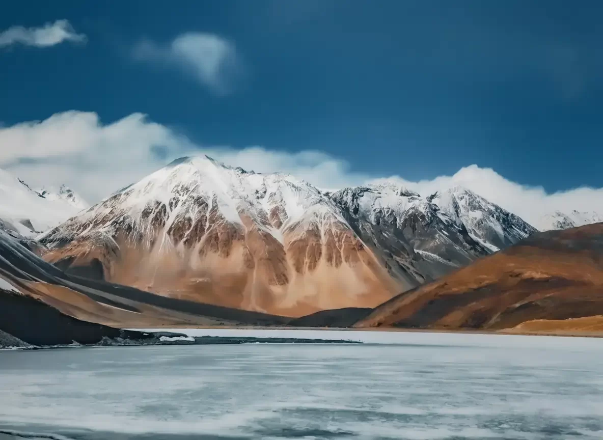 Icy Pangong Lake at Pangong Tso Ladakh during winter clear skies, featuring snow peaks and terraced mountains, perfect adventure Ladakh tour package. 