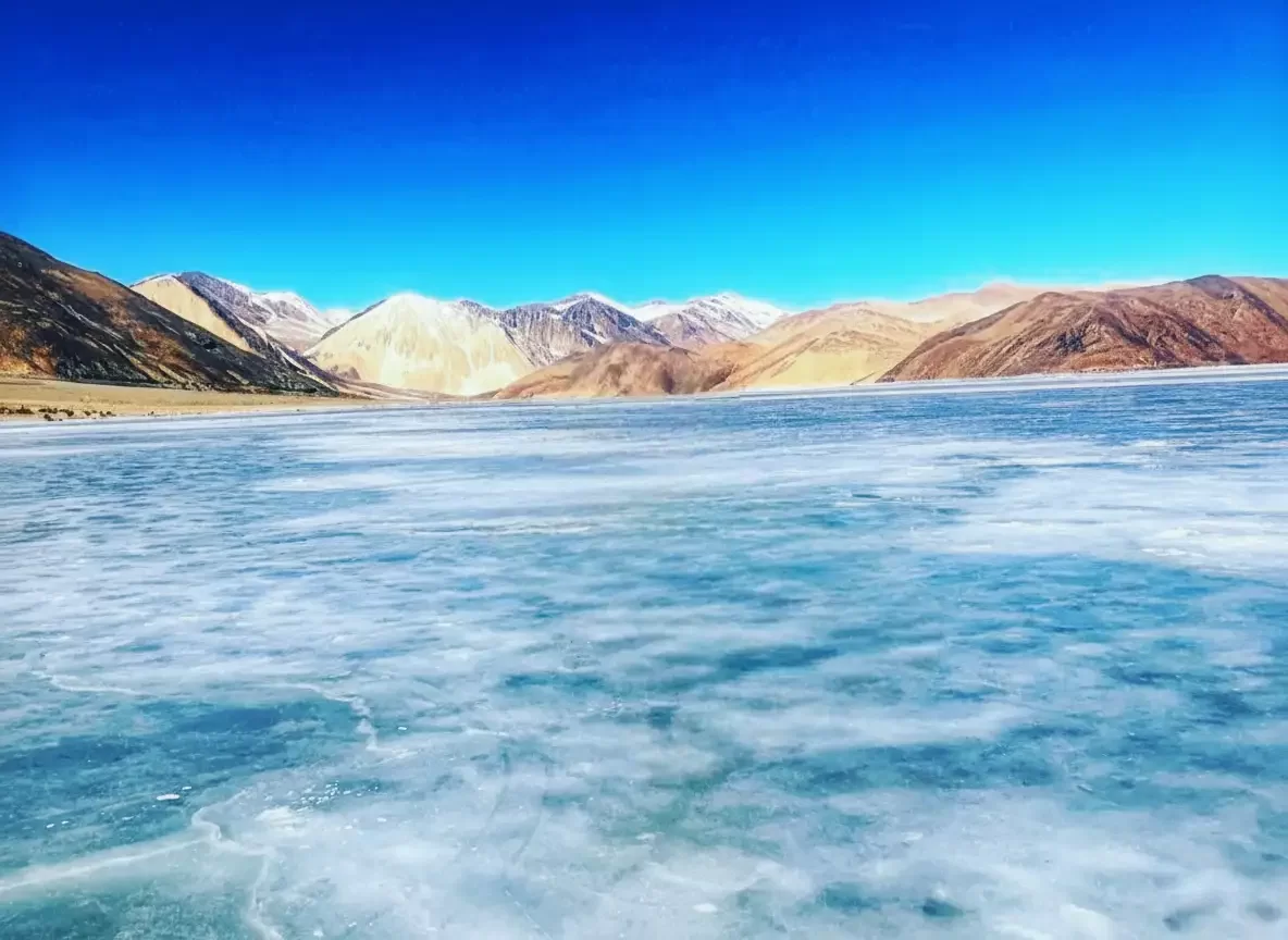 Pristine Pangong Lake at Pangong Tso Ladakh in winter blue hour, featuring icy expanse and rugged snowy mountains, perfect adventure Ladakh tour package.
