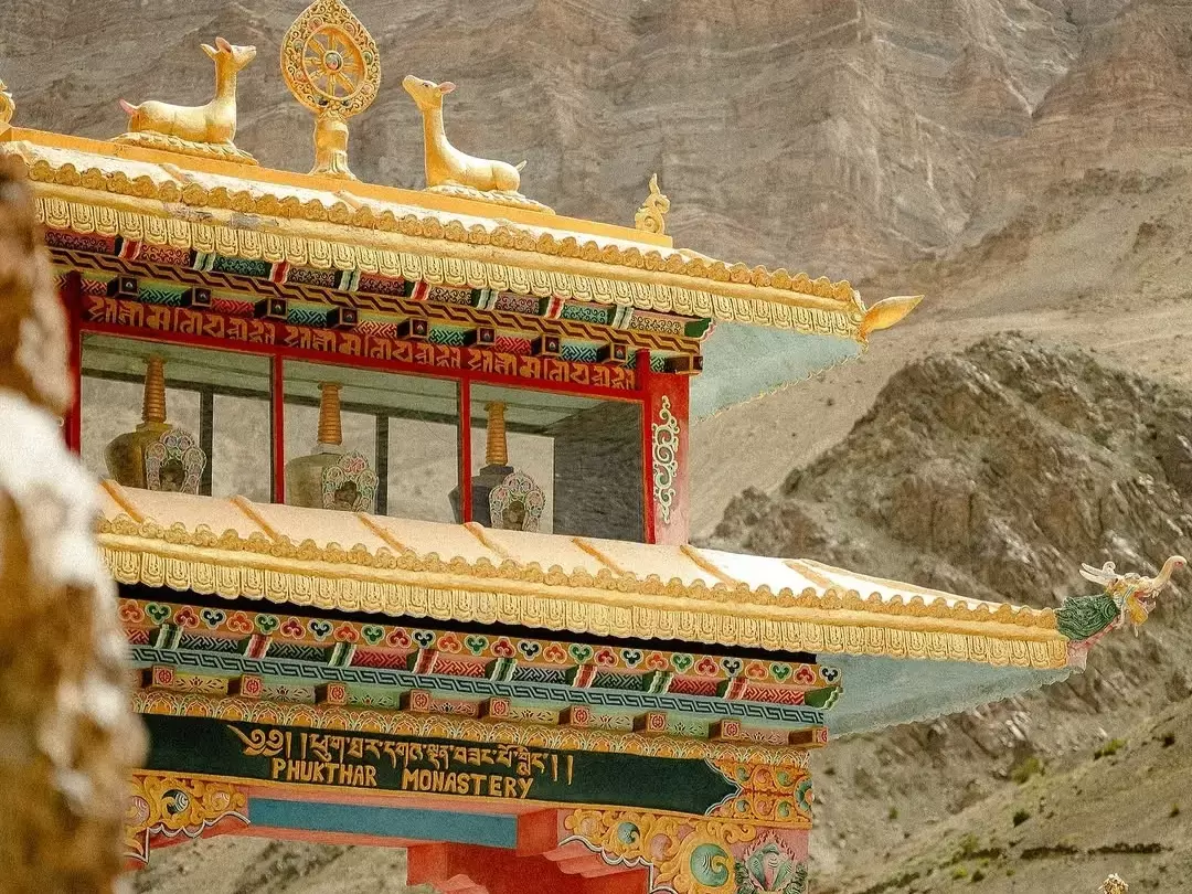 Phuktal Gompa (Phugtal Monastery) in Zanskar Valley Ladakh close-up of ornate golden roof with deer figures, bells, red pillars and Tibetan script against rugged cliff backdrop, perfect Ladakh tour package