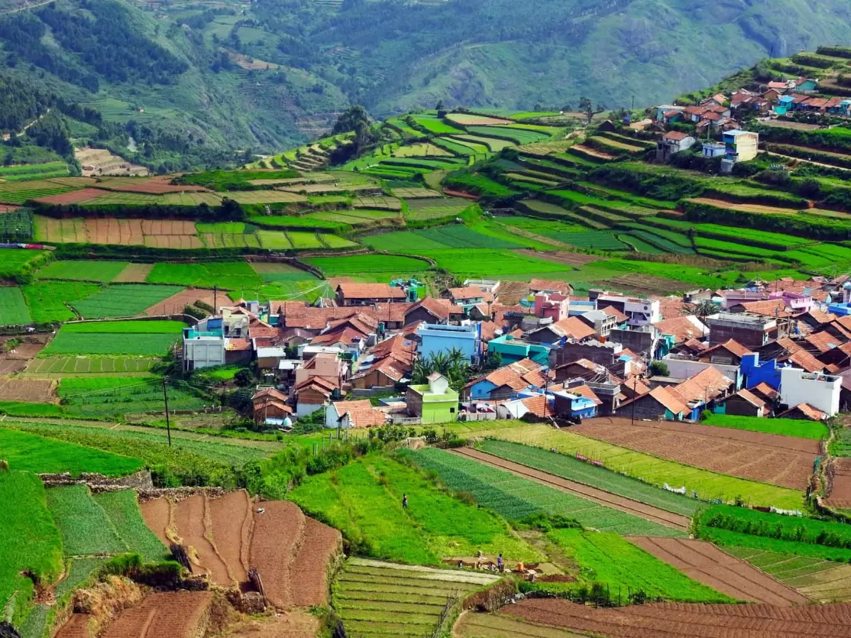 Panoramic view of Poombarai village at Kodaikanal during misty morning, featuring terraced fields, colorful houses, mountains, perfect adventure experience Tamil Nadu tour packages.