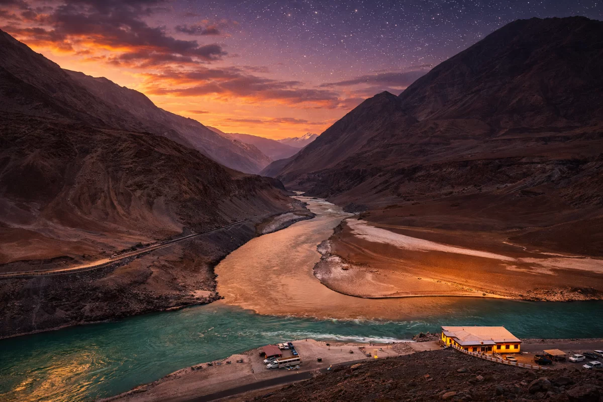 Sangam Leh Ladakh at breathtaking sunset: confluence of turquoise Zanskar and Indus rivers winding through dramatic mountain valley with orange sky and starry twilight