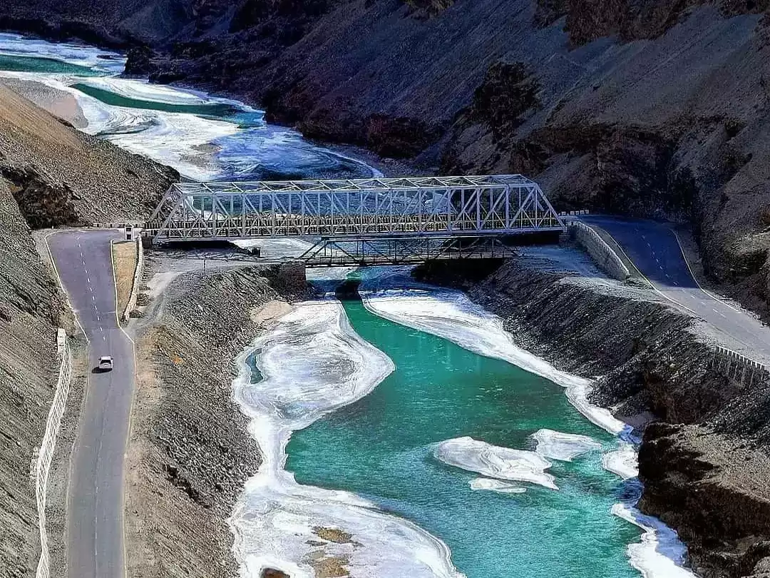 Sangam bridge over Indus Zanskar at Leh Ladakh during clear day, featuring turquoise rivers gorge road mountains ice flows, perfect adventure Ladakh tour package.