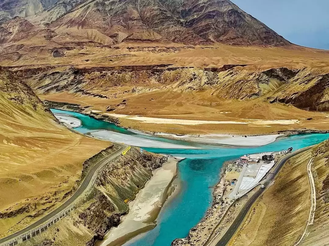 Sangam Indus Zanskar confluence at Leh Ladakh during partly cloudy day, featuring turquoise rivers valley mountains road, perfect adventure Ladakh tour package.