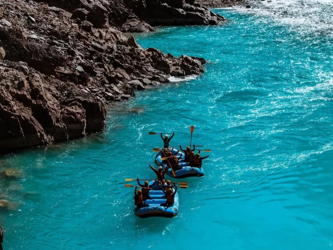 River rafting at Sangam Leh Ladakh during sunny day, featuring blue rafts turquoise waters rocky gorge paddlers, perfect adventure Ladakh tour package.
