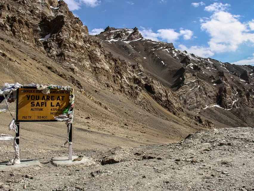 Sam La pass BRO signboard 4370m prayer flags barren rocky cliffs snow peaks blue skies Ladakh, lesser-known high-altitude pass Nyoma-Chumathang route Tso Moriri loop scenic BRO engineering feat