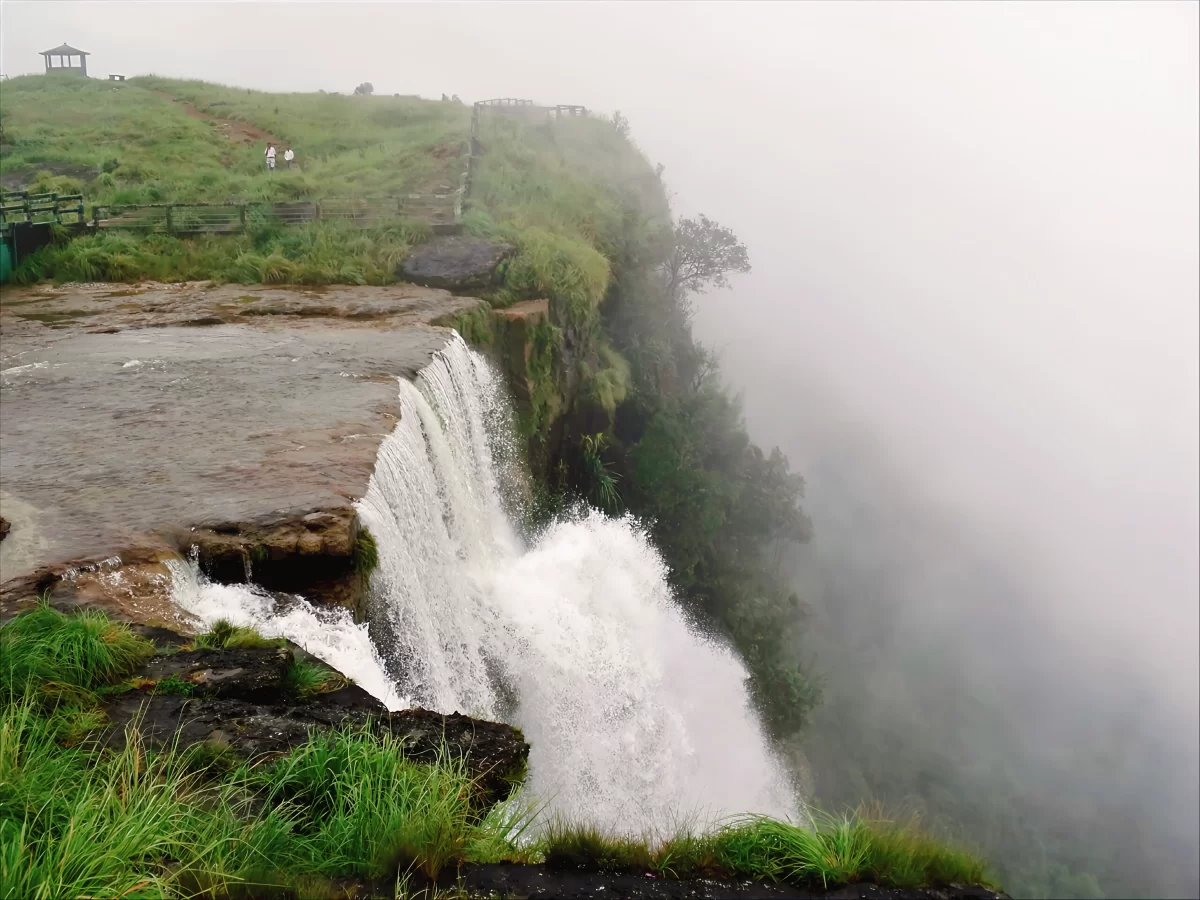 Seven Sisters Falls Cherrapunji during misty morning, featuring cascading waterfall cliff edge viewing platform green hills clouds, perfect nature adventure Cherrapunji Meghalaya tour package.
