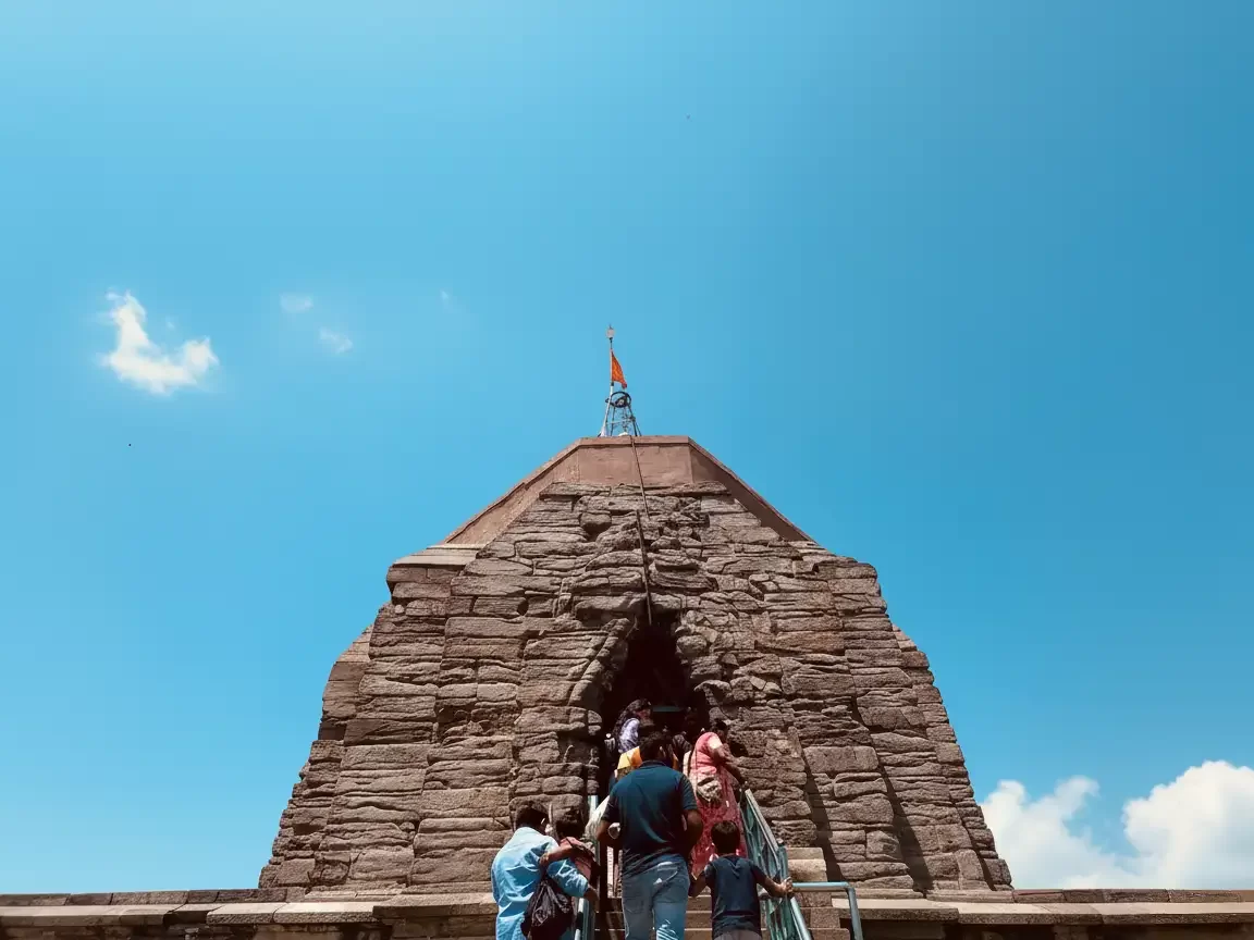 Shankracharya Temple Srinagar during sunny day Jammu Kashmir, featuring tiered stone shikhara saffron flag devotees blue sky backdrop, perfect Jammu Kashmir tour packages. 