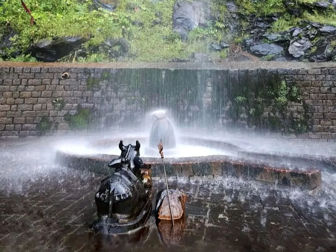 Shri Anjani Mahadev Mandir in Manali, Himachal Pradesh, featuring a natural Shiva lingam beneath cascading waterfall water with a Nandi statue in the foreground, a revered spiritual site included in Himachal Pradesh tour packages.