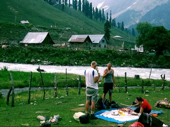 Picnic by Sindh river at Sonamarg during misty day, featuring snowy mountains & cottages, perfect romantic experience Kashmir tour packages.
