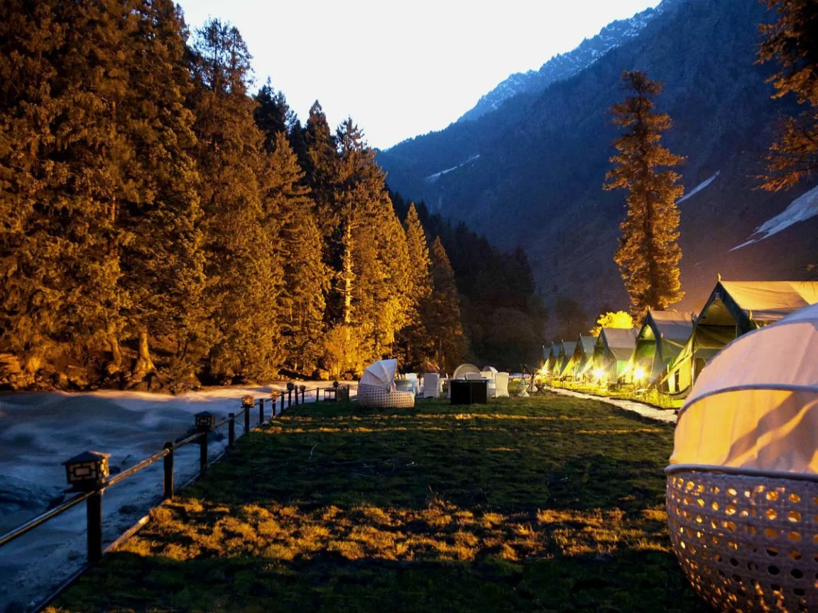 Glamping tents at Sonamarg during twilight, featuring pine trees & snowy mountains reflections, perfect romantic experience Kashmir tour packages.