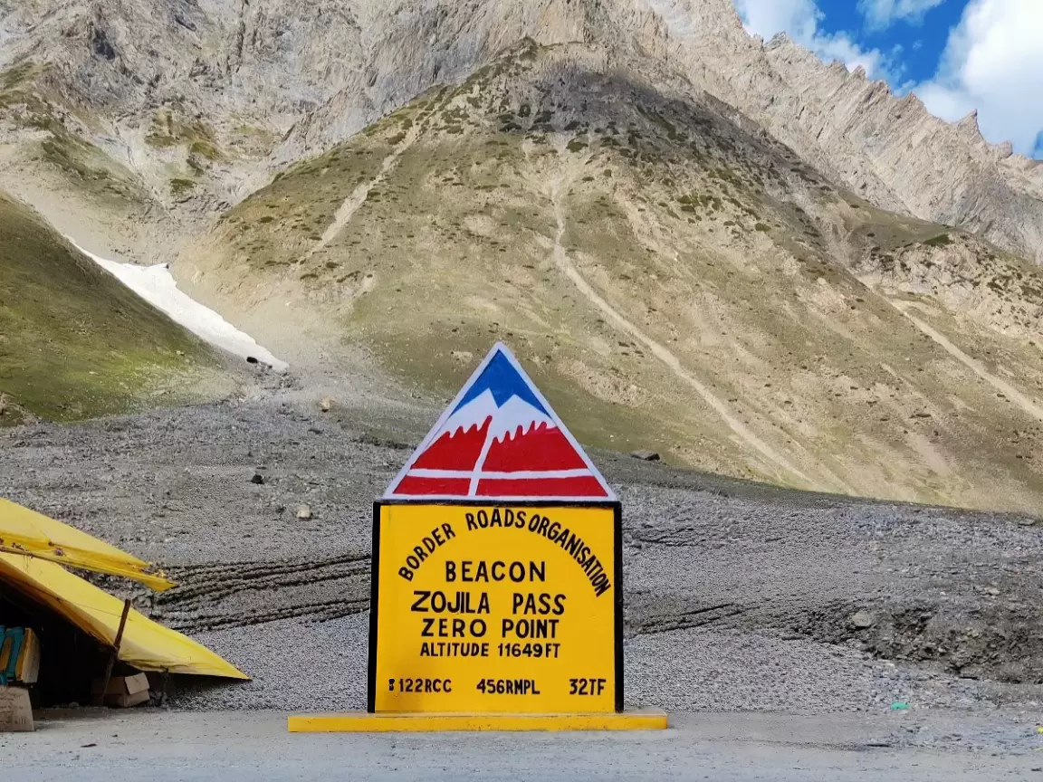 Zojila Pass sign at Sonamarg route during sunny day, featuring border roads board & mountains, perfect adventure experience Kashmir tour packages. 
