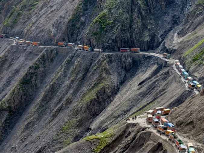 Colorful trucks convoy at Sonamarg road during cloudy day, featuring steep cliffs & mountain pass, perfect adventure experience Kashmir tour packages.