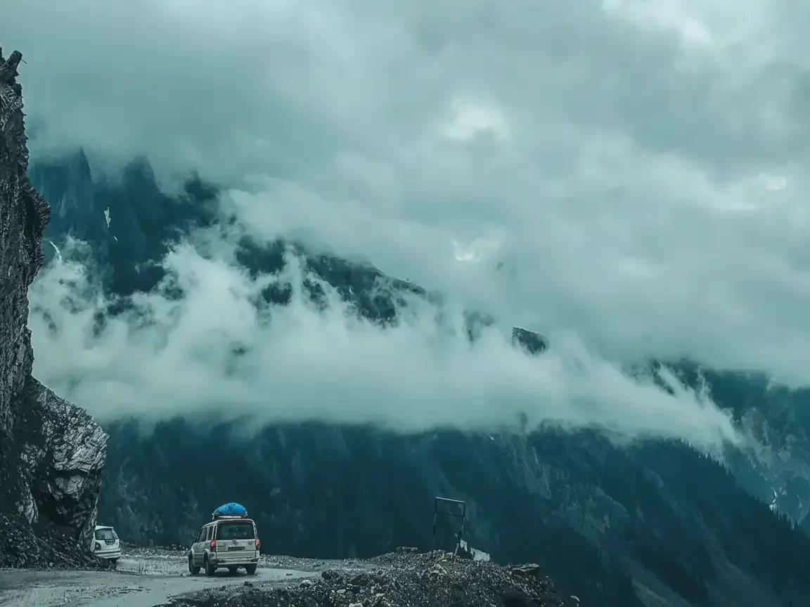 Jeep drive at Sonamarg road during misty weather, featuring snowy mountains & foggy cliffs, perfect adventure experience Kashmir tour packages. 