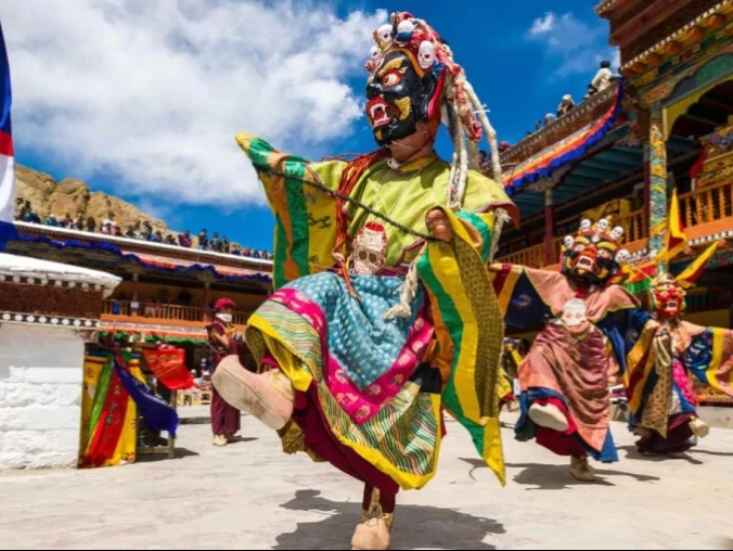 Masked cham dancer at Spituk Gustor Festival in Ladakh under blue sky, featuring colourful monastery courtyard, perfect Ladakh cultural tour package