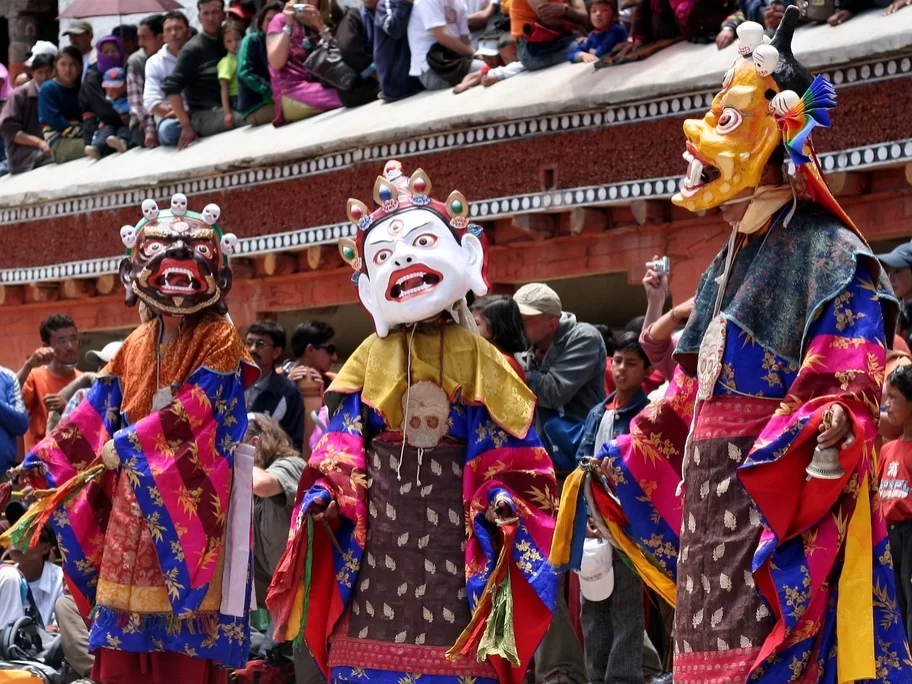 Mask dance performers at Spituk Gustor Festival in Ladakh during daytime, featuring colourful robes and crowd, perfect Ladakh cultural tour package