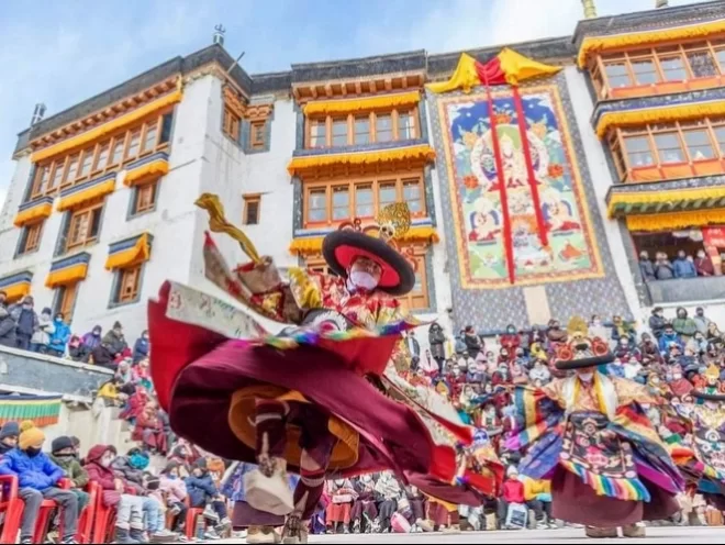 Cham dance at Spituk Gustor Festival in Ladakh during daytime, featuring colourful monastery facade and crowd, perfect Ladakh cultural tour package
