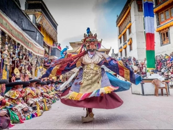 Spituk Gustor Festival dance at Leh Ladakh during cloudy day, featuring masked dancer prayer flags monastery crowd, perfect cultural Ladakh tour package.