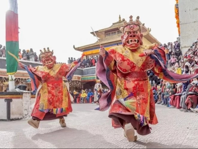 Masked monks performing cham dance at Spituk Gustor Festival in Ladakh, featuring vibrant robes and monastery crowd, perfect Ladakh cultural tour package