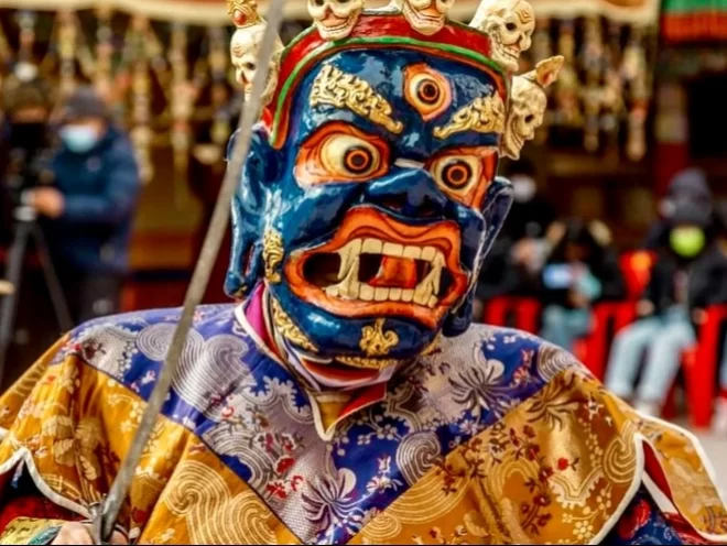 Fierce deity mask at Spituk Gustor Festival in Ladakh during daytime, featuring ornate headgear and silk robes, perfect Ladakh cultural tour package.